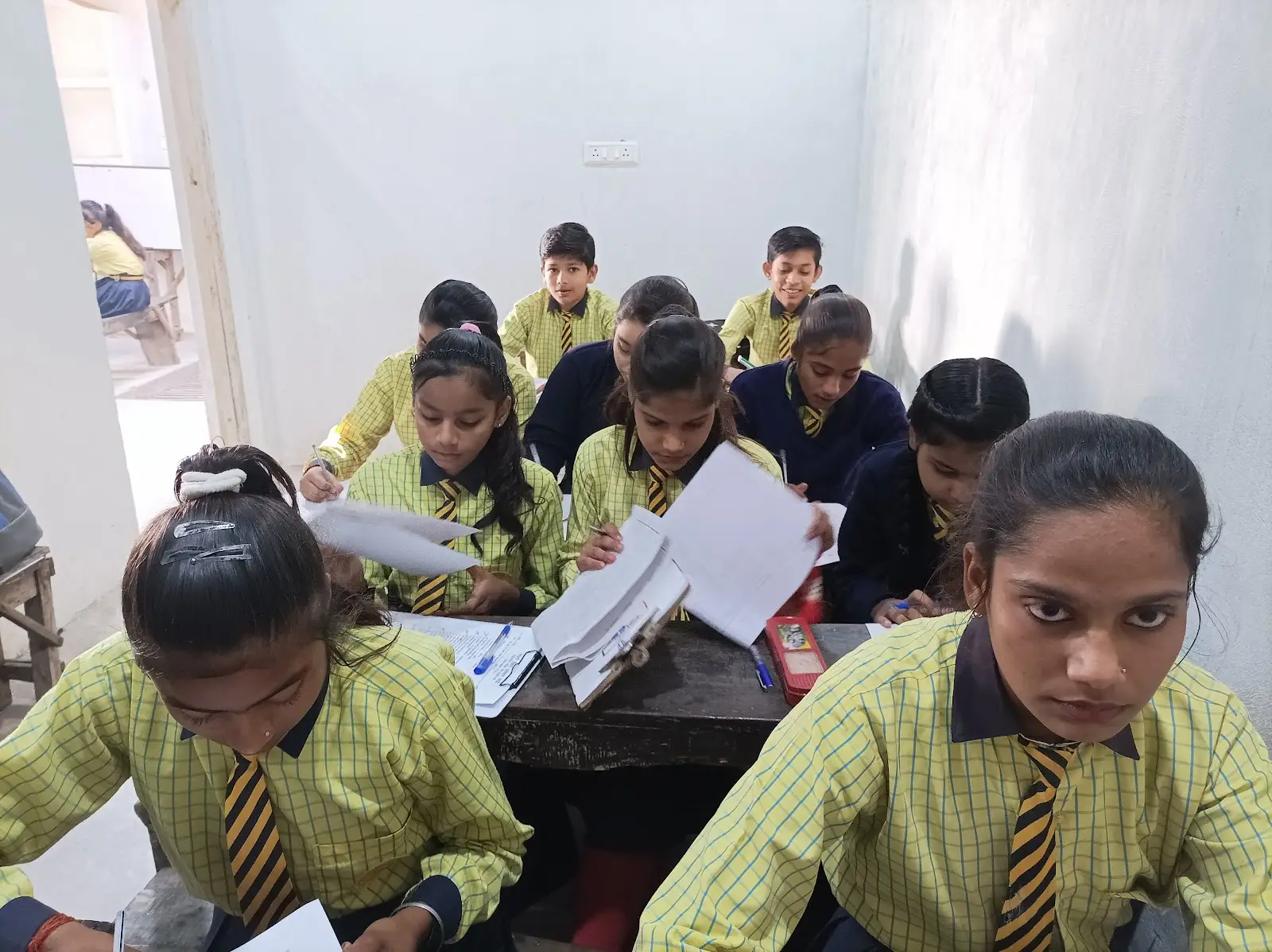वर्दी पहने बड़े विद्यार्थी कक्षा में कागज़ों पर काम करते हुए